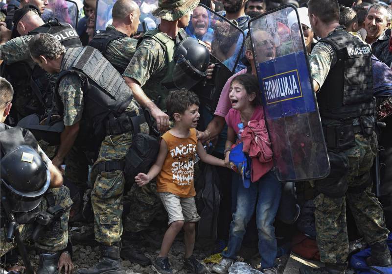 21/8/15: Παιδιά μεταναστών ξεσπούν σε κλάματα στην ελληνική πλευρά των συνόρων, απέναντι σε αστυνομικούς της ΠΓΔΜ, κοντά στην Γευγελή. - EPA/GEORGI LICOVSKI