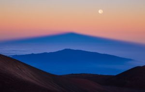 H σκιά του Manua Kea, της υψηλότερης κορυφής της Χαβάης διακρίνεται στον ορίζοντα μαζί με το φως του ανατέλλοντος ηλίου και το φεγγάρι που δεν έχει δύσει ακόμη. Φωτογραφία © Sean Goebel 